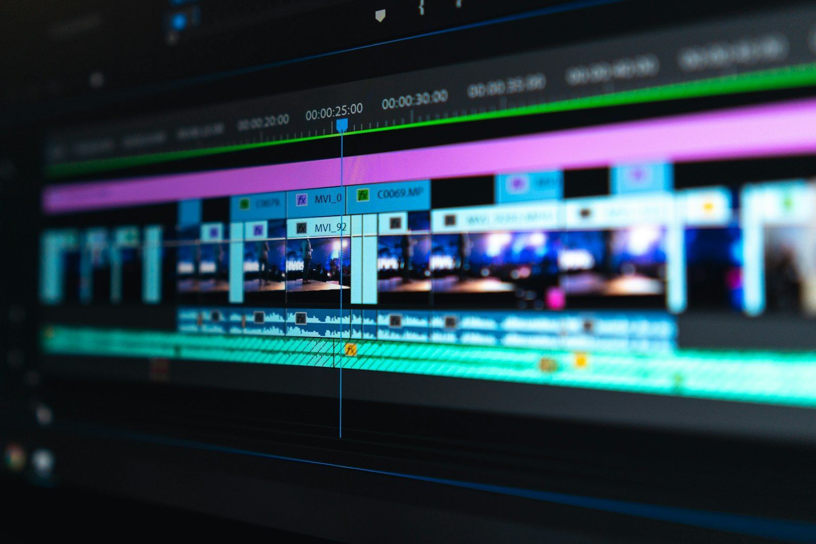 Close-up of a video editing timeline with colorful clips and audio tracks on a dark monitor
