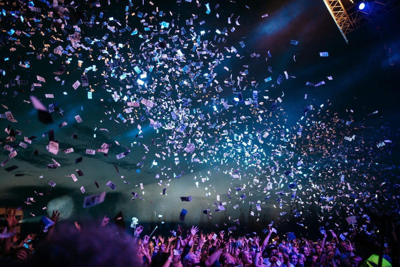 Confetti falling over a cheering crowd with raised hands under stage lights