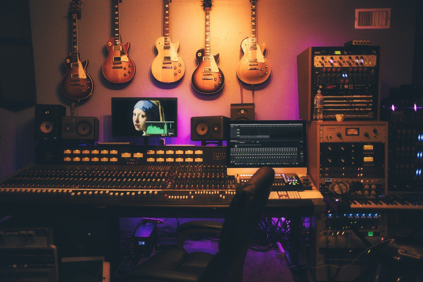 Recording studio with a mixing console, outboard gear and electric guitars hanging on the wall