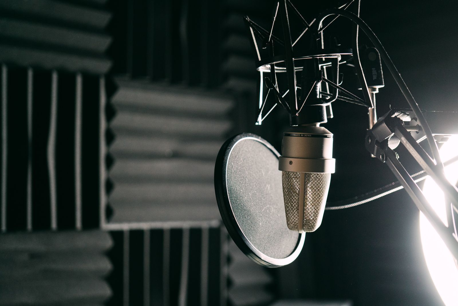 Condenser microphone with a pop filter in a dark recording booth lined with acoustic foam