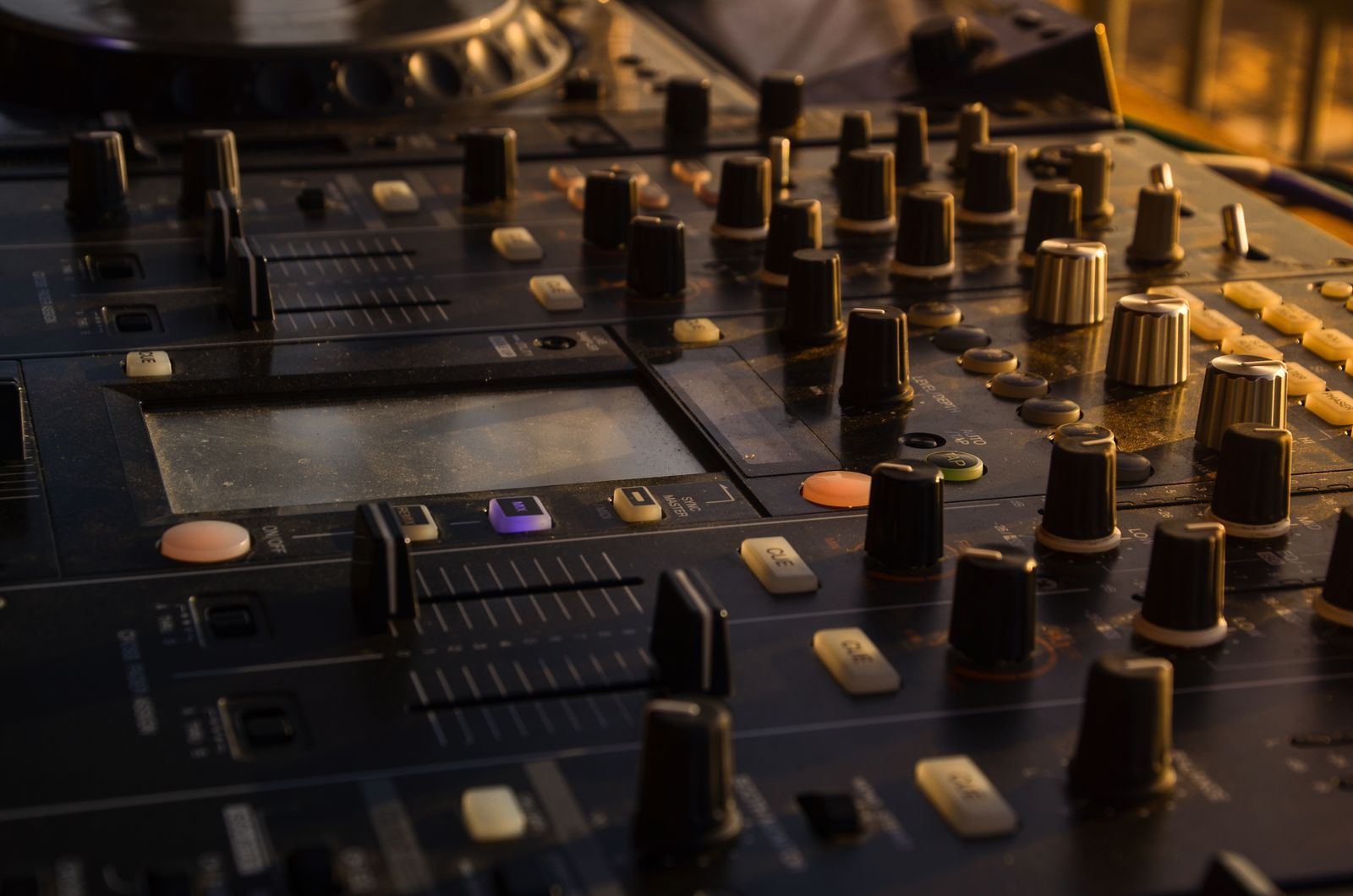 Close-up of a DJ mixer with black knobs and faders lit by warm evening light