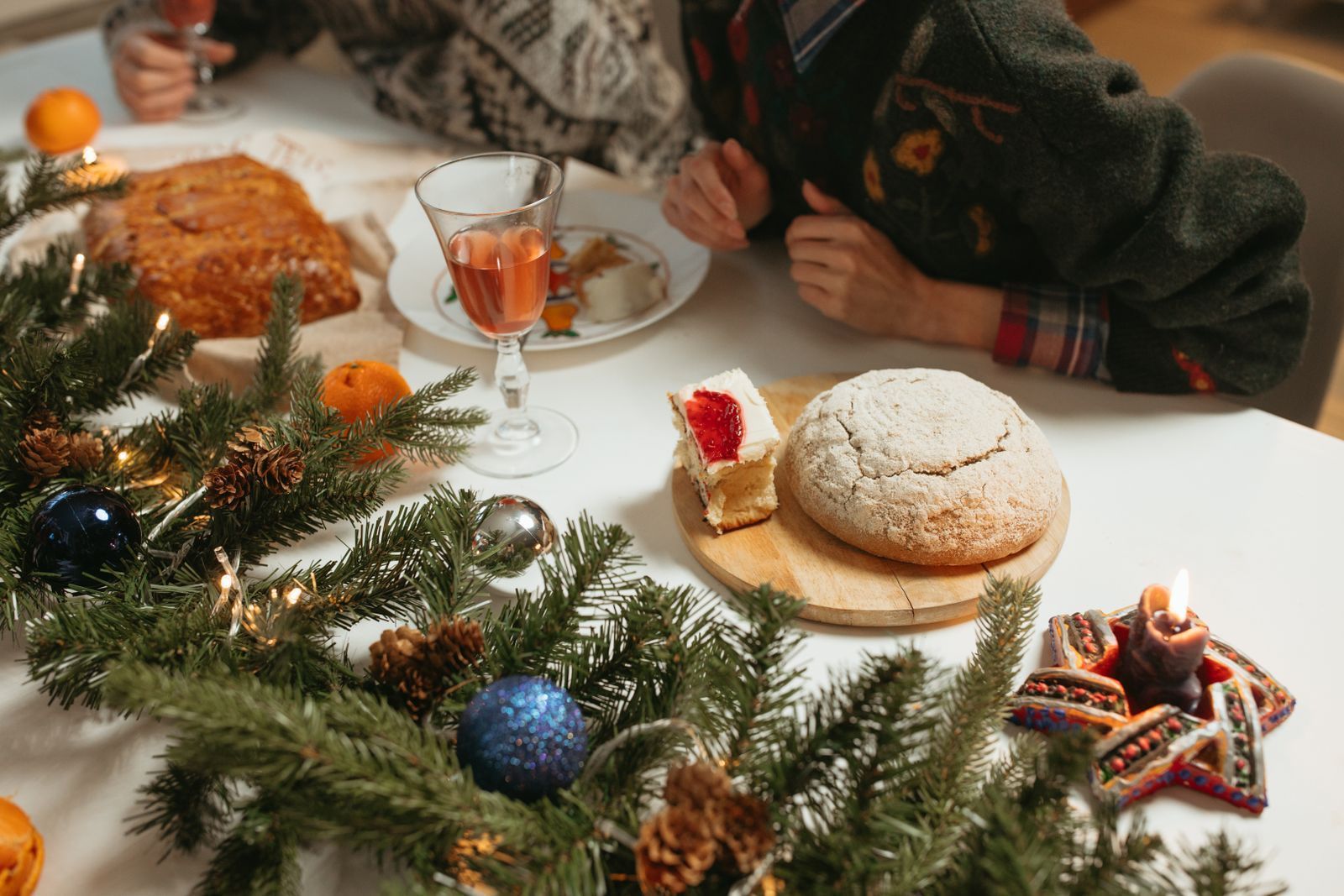 Dinner table with a glass of rosé, bread, pine branches and a lit candle while guests talk