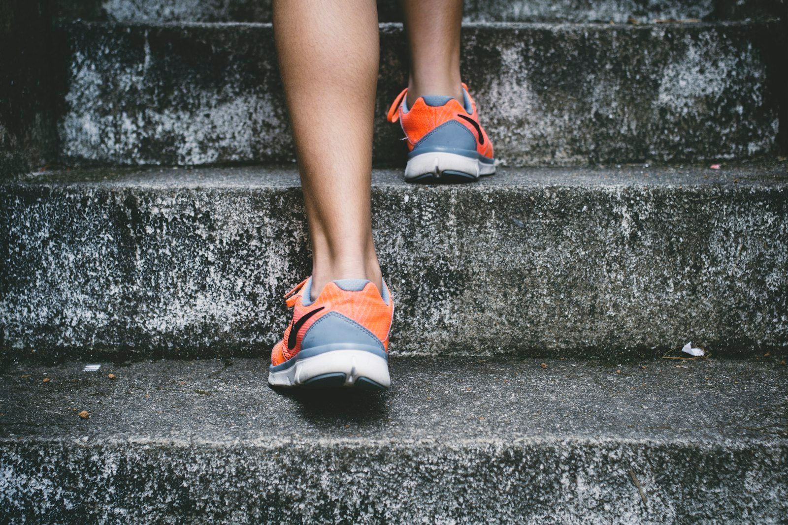 Close-up of a runner's orange and grey shoes climbing concrete steps