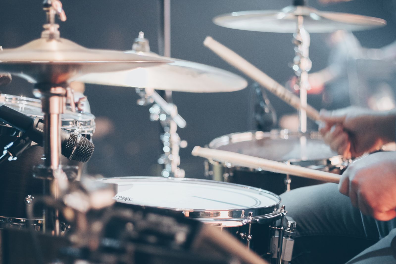 Drummer playing a kit with sticks, cymbals and a microphone in the foreground