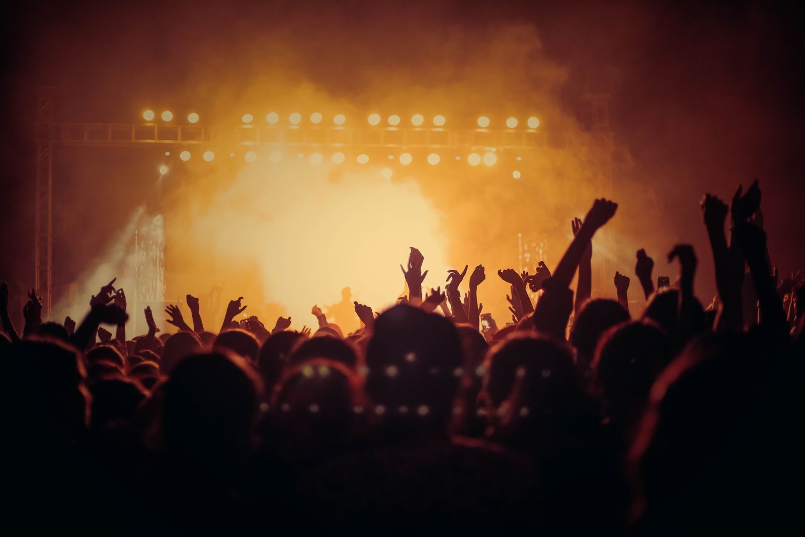 Crowd with raised hands facing a stage lit by golden lights and haze at a live concert