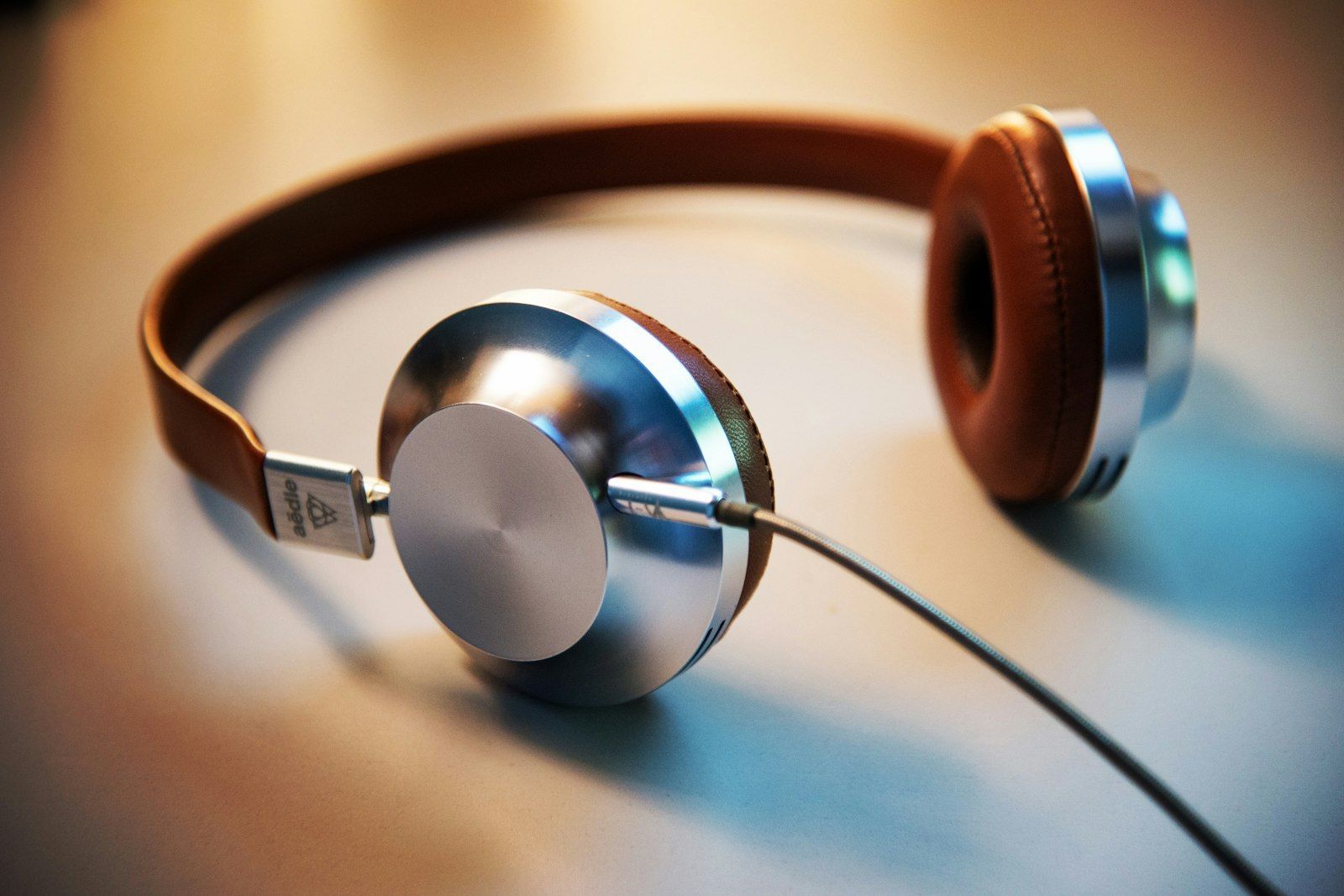 Brown leather and brushed aluminium over-ear headphones resting on a table with a cable trailing away