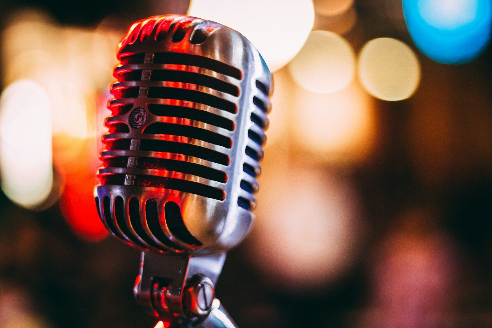 Close-up of a chrome vintage microphone with colorful blurred stage lights behind it